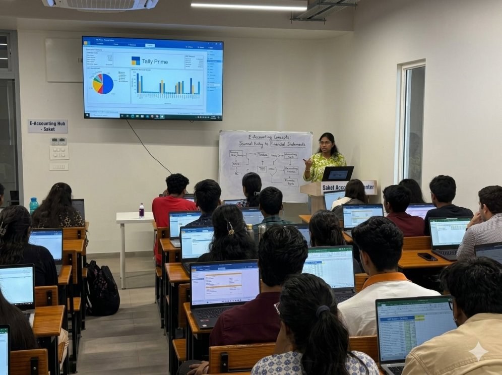 A modern E-Accounting classroom in Saket with an instructor presenting digital financial concepts to rows of students. Students follow along on individual laptops displaying accounting spreadsheets.